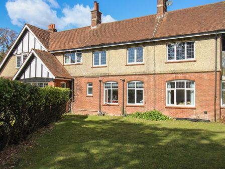 A two story house with brick lower walls and pebble dash upper walls with multiple windows and a hedge in front at Deer Leap Cottage in Moreton
