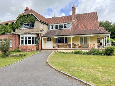 A house with ivy on one side a paved driveway and a porch with wooden furniture at Deer Leap House in Moreton
