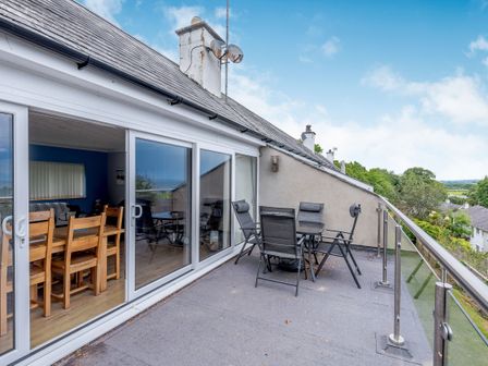 A balcony with a table and chairs outside sliding glass doors overlooking trees and houses at 17 Glyn Y Marian Llanbedrog near Abersoch