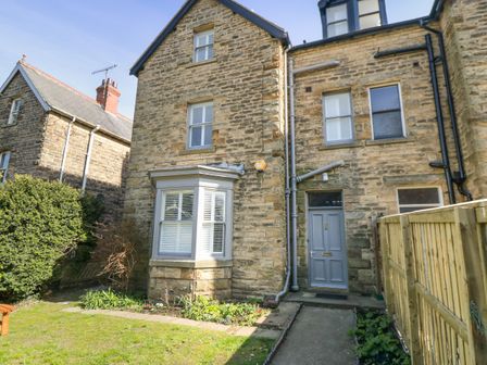 A stone exterior house with a blue front door and white window shutters with a garden and wooden fence at Hazeldene in Sleights