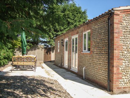 An outdoor area with a gravel ground and a paved pathway next to a building with pebble and brick walls and a bench with an umbrella at The Old Barn in Walcott