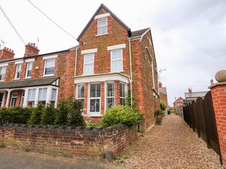 A row of brick houses with a gravel pathway and a low brick wall in front at Troon Cottage in Hunstanton
