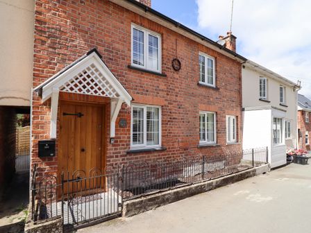 The exterior of a red brick house with white framed windows wooden front door and black metal fence at Tan Y Ddol in Llanfair Caereinion