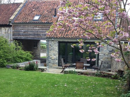 A garden with green grass and a stone house with wooden chairs and a table at Willow Barn in Shapwick