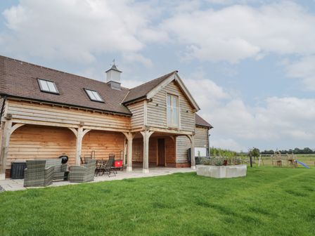 A wooden holiday lodge with outdoor seating and a children's play area on a lawn at Hallgarth Farm Holiday Lodge in Peopleton