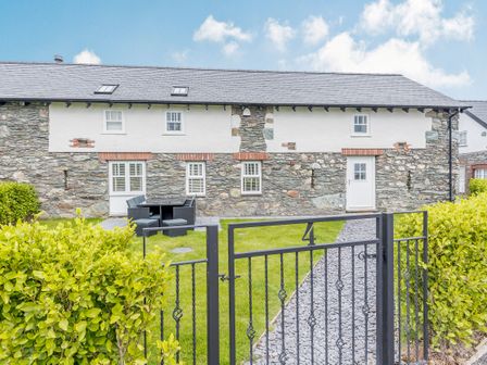 A stone and white exterior house with a black metal gate and a stone path with green lawn and outdoor table and chairs at Sgubor in Valley