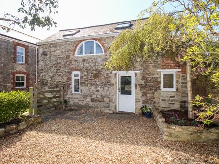 A stone cottage with a white door and windows a wooden gate and gravel driveway at Little Brook in Nottington near Weymouth