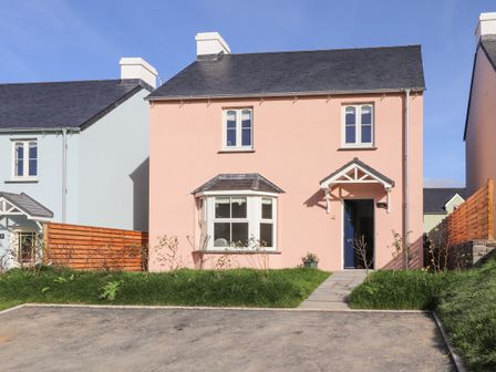 A pink two-story house with a blue door and a driveway at 4 Llain yr Eglwys in Newport Pembrokeshire