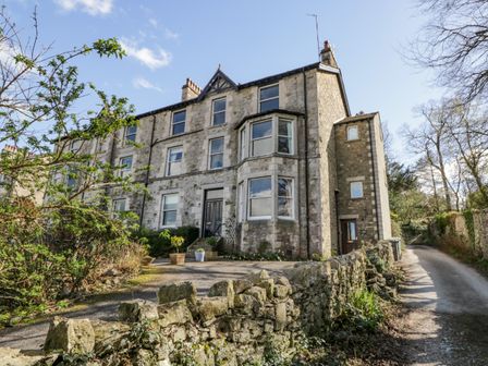 A stone house with multiple windows and a stone wall beside a narrow road at Crows Nest in Arnside