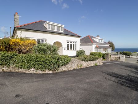 Two white houses with tiled roofs by a paved road and stone walls with bushes by the sea at The Nook in Benllech