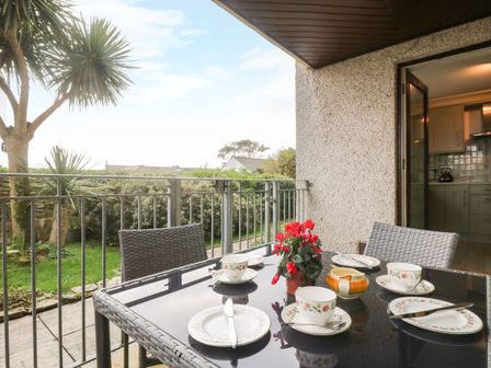 An outdoor patio dining area with a glass table set for tea and red flowers at The Wesley Apartment in Falmouth