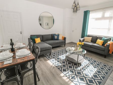 A living room with two gray sofas and a dining table set with plates at Pebble Cove in Amble