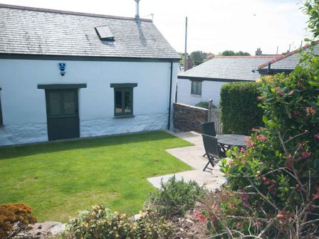 A garden with green grass and patio furniture beside a white building at Apple Barn in Crantock