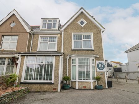 The exterior of a pebble dash house with white framed windows and a sign that reads The Three Tees in Newquay