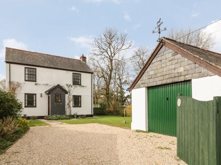 A white two-story house with a gray roof and a green garage door with a green gate outside at Thrushel Cottage in Lifton