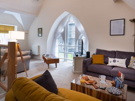 A living room with a yellow armchair gray sofa and wooden coffee tables at The Belfry in Windermere