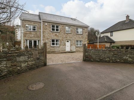 A stone house with white windows and door behind a stone wall and open gate at About Time Cottage in Parkend