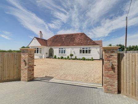 The front of a white house with a red tiled roof a gravel driveway and a wooden fence at The Little Paddock in Malmesbury