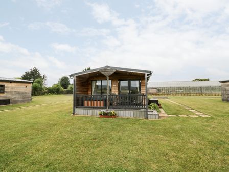 A wooden cabin with a small porch and railing on a grass lawn at Cotswold View 3 in Bretforton near Evesham