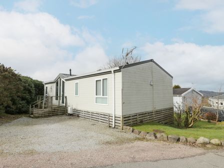 A single story mobile home with windows and a small porch with steps on a gravel and grass lot at Oyster Bay Lodge in Dalbeattie