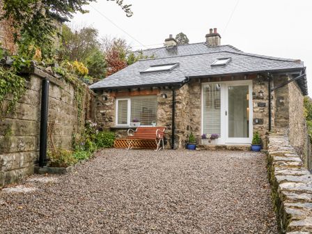 A small stone house with a gravel driveway a wooden bench and plants at Horncop Nook in Kendal