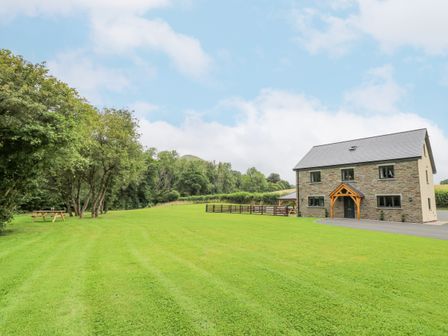 A stone house with a pitched roof on a large lawn with trees and a picnic table at Talarddu Cottage in Builth Wells