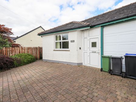 The exterior of a white cottage with a brick driveway and three trash bins at Limhus Cottage in Keswick