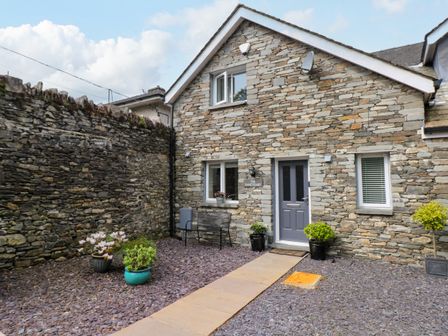 A stone house exterior with a gray door and windows a pathway and potted plants at The Sanctuary in Windermere