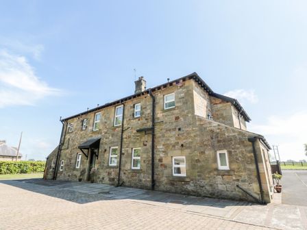A stone exterior building with multiple windows and paved ground at Deanrise in Shilbottle near Alnwick