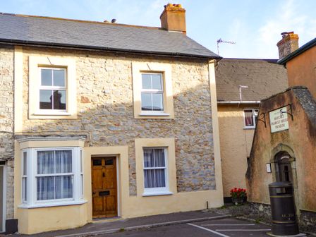 Stone house with wooden door and bay window next to sign for Watchet Market House Museum in Watchet