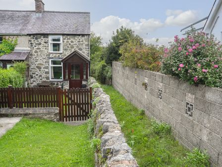 A stone house with a brown wooden gate and fence and a garden with plants and flowers at Pen Dinas in Minffordd near Bangor