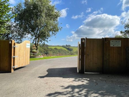 Open wooden gates on a driveway with a tree and green fields in the background at Woodhall in Cardinham
