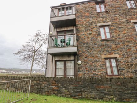 Exterior of a stone building with balconies and metal green chairs at 2 Chandlers Yard in Burry Port