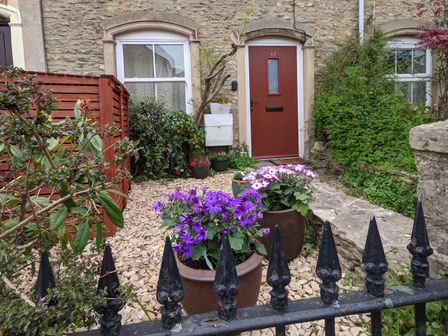 Front garden with flower pots and a red door on a stone house at The Cottage in Tetbury