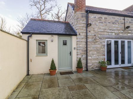 A stone and plaster exterior with a green door and window and potted plants on the patio at Magnolia Barn in Mark