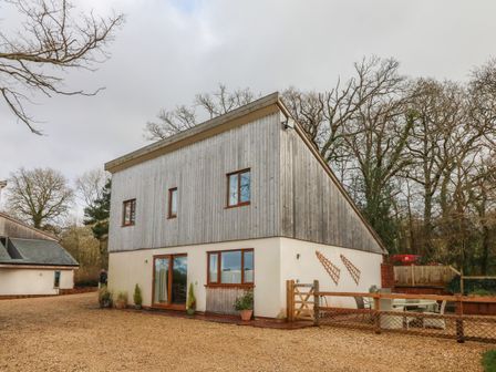 A two-story house with wooden upper walls and cream lower walls beside a gravel driveway and outdoor seating area at The Outlook in Crowcombe