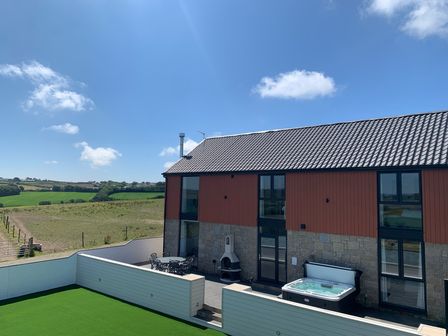 A modern house with a patio, outdoor dining table, hot tub, and green lawn in a rural setting at Valley View in Mullion