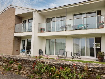 Exterior view of a two story building with balconies and patio areas with chairs and tables and flowers in pots at 7 Europa Court in Mawgan Porth