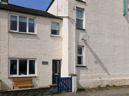 Exterior of a white two-story house with multiple windows a blue door and a small blue gate with a bench outside at Inglewood in Keswick