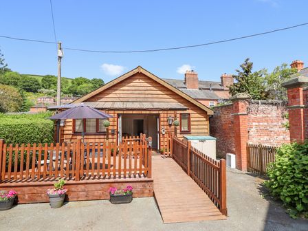 A wooden house with a ramp and fenced patio with an umbrella and potted plants at Varley Villa in Newtown