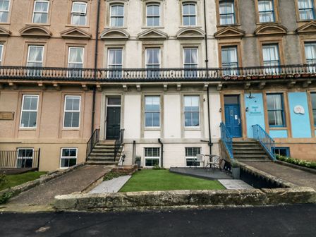 The front exterior of a row of terraced houses with steps and ramps leading to doors with a small garden area in front at Sandsend Sunset View Whitby