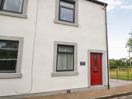 Exterior view of a white house with three windows and a red door at Herdwick Heaf in Ennerdale