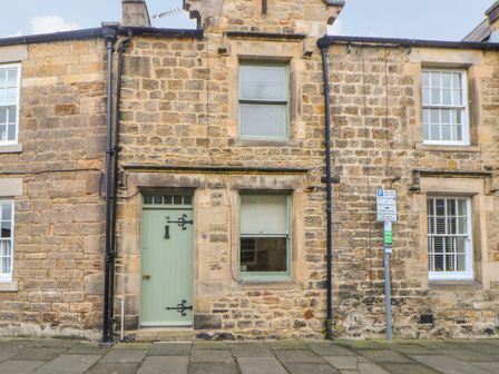 A stone house facade with a green door and two windows on a street with a parking sign at Chapel Cottage in Corbridge