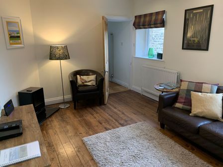 A living room with a black armchair and sofa with pillows a floor lamp and a small table at A Stone's Throw in Alnmouth