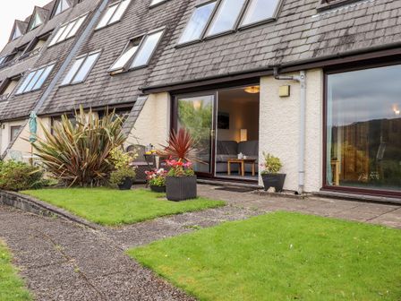 The exterior of a building with large windows and patio doors opening to a garden with plants and a paved path at Pavey Ark in Ambleside