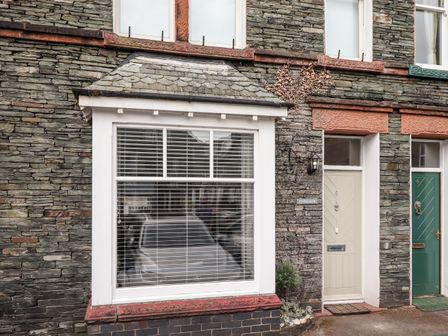 The exterior of a stone house with a large white-framed window and two doors one white and one green at Stanegarth in Keswick