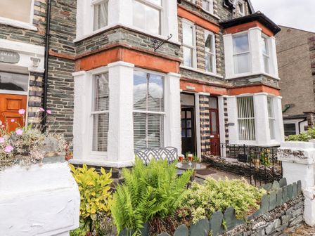 Exterior of a house with large bay windows a small garden and table with two drinks at Oakhurst in Keswick