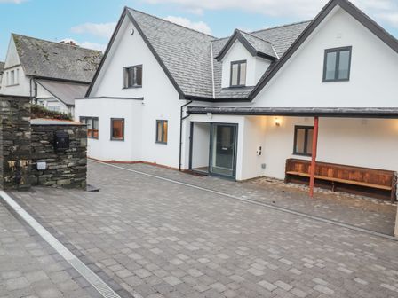 A paved driveway in front of a white two-story house with a bench under a covered area at Garth Hill House in Ambleside