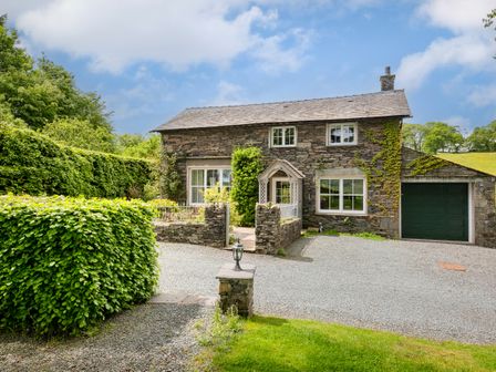 A stone house with a gravel driveway green hedges and a garage at Hilltop At Hawkshead Hill in Hawkshead