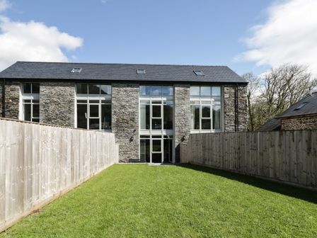 A garden with grass and wooden fences in front of a stone building with large windows at 2 Pensyflog Barns in Porthmadog